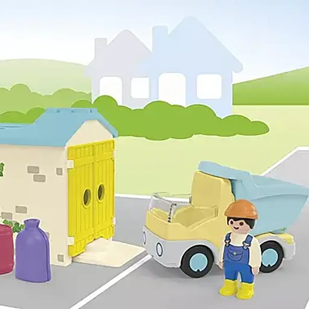 Playmobil Junior construction scene features pastel dump truck, yellow-doored garage and bright shape pieces arranged on a simple neighborhood backdrop with soft houses and greenery.