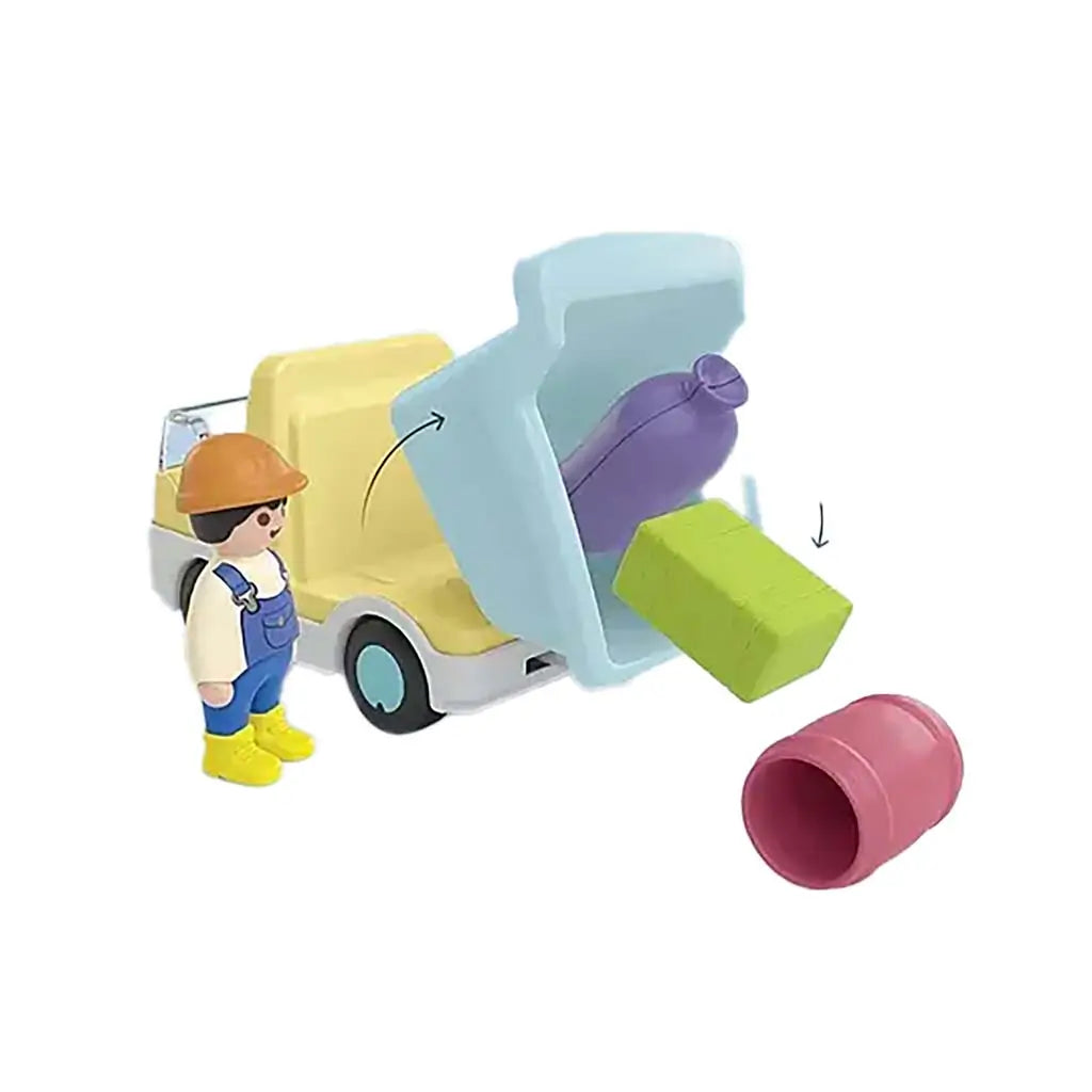 Playmobil Junior unloading action shows blue dump bed lifting to release colorful shape pieces while a smiling builder figure stands nearby ready for toddler-friendly construction play.