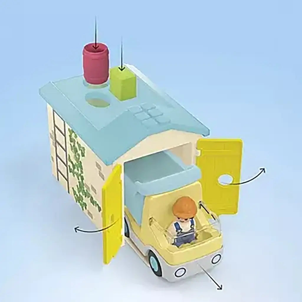 Playmobil Junior top view shows yellow garage doors opening as colorful shapes drop into roof slots while a pastel dump truck and builder figure encourage beginner construction play.
