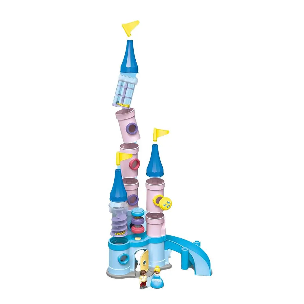 A completed Playmobil Disney castle playset rises from pastel pink and blue tubular pieces topped with yellow flags, including a clear spiral-ramp section and small character figures arranged at its base.