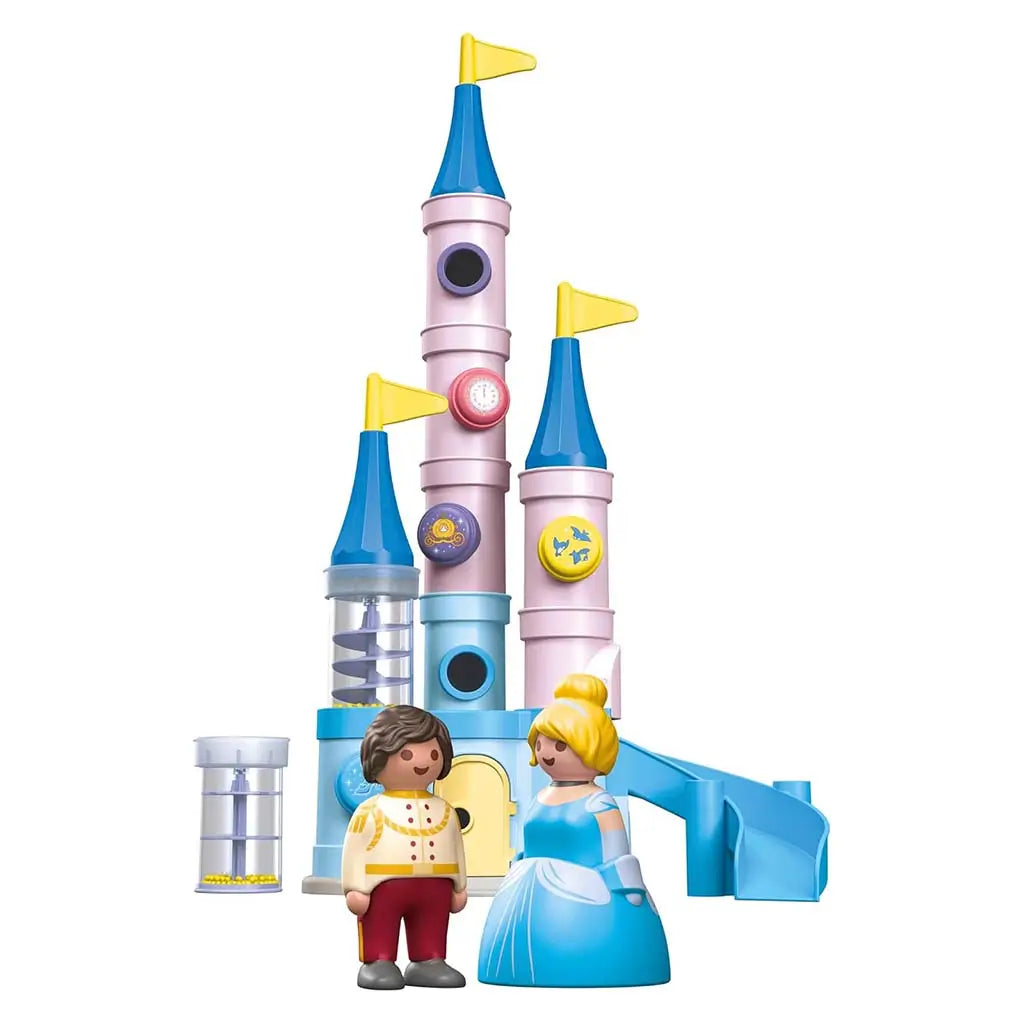 A pastel Playmobil Disney castle stands with tall blue and pink towers, yellow flags, a slide, and a clear spiral-ramp tube beside Cinderella and the Prince figures posed at the base for imaginative play.
