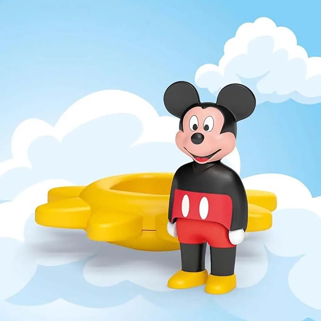 Playmobil Junior Mickey Mouse figure stands beside a detachable yellow sun spinner against a soft cloud background, emphasizing simple imaginative play and easy handling for little hands.