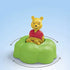 Disney Playmobil Junior Winnie the Pooh figure seated on a bright green rounded platform with smooth curved edges, shown rotating in a simple blue background that highlights its playful motion.