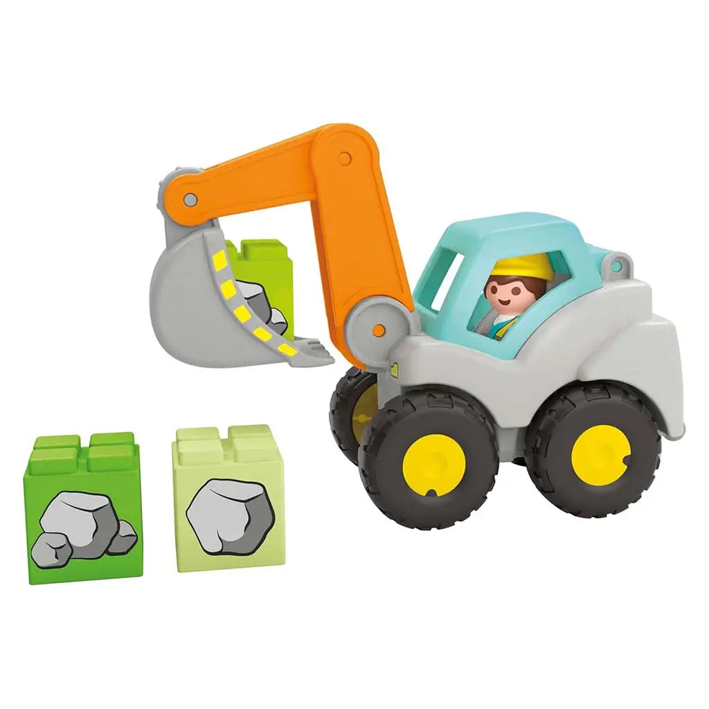 Playmobil Junior excavator toy features a gray body, bright orange digging arm, large black wheels with yellow hubs, and two blocky rock pieces, emphasizing simple construction play on a clean white background.