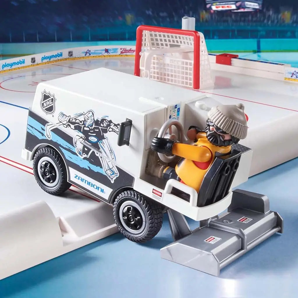 Playmobil NHL Zamboni toy in white plastic with printed graphics and textured wheels driving on the smooth rink surface near the red goal crease inside a brightly lit arena setting.