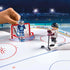 Playmobil NHL figurines on a smooth white rink illustrate a shooting action scene near the red goal crease, with rotating goalie and skater pieces positioned in a detailed arena setting.