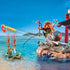 Playmobil pirate raft scene showing bright coral, red-haired figure with map, log raft, firing cannon and clear tropical water stretching toward distant green islands under a vivid blue sky.