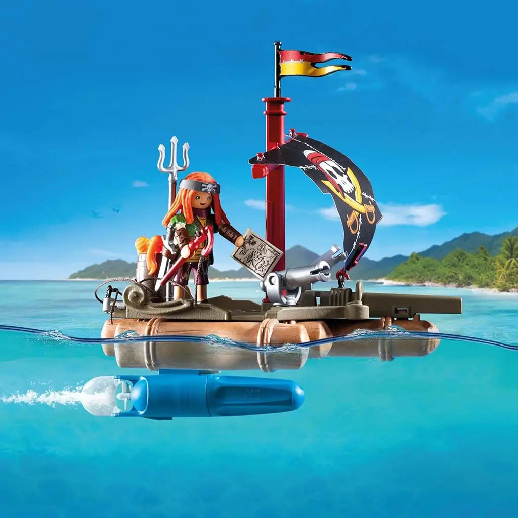 Playmobil pirate raft floating on clear turquoise water with red mast, black skull sail, orange-haired figure holding map and hook, plus a visible blue underwater motor near the tropical shoreline.