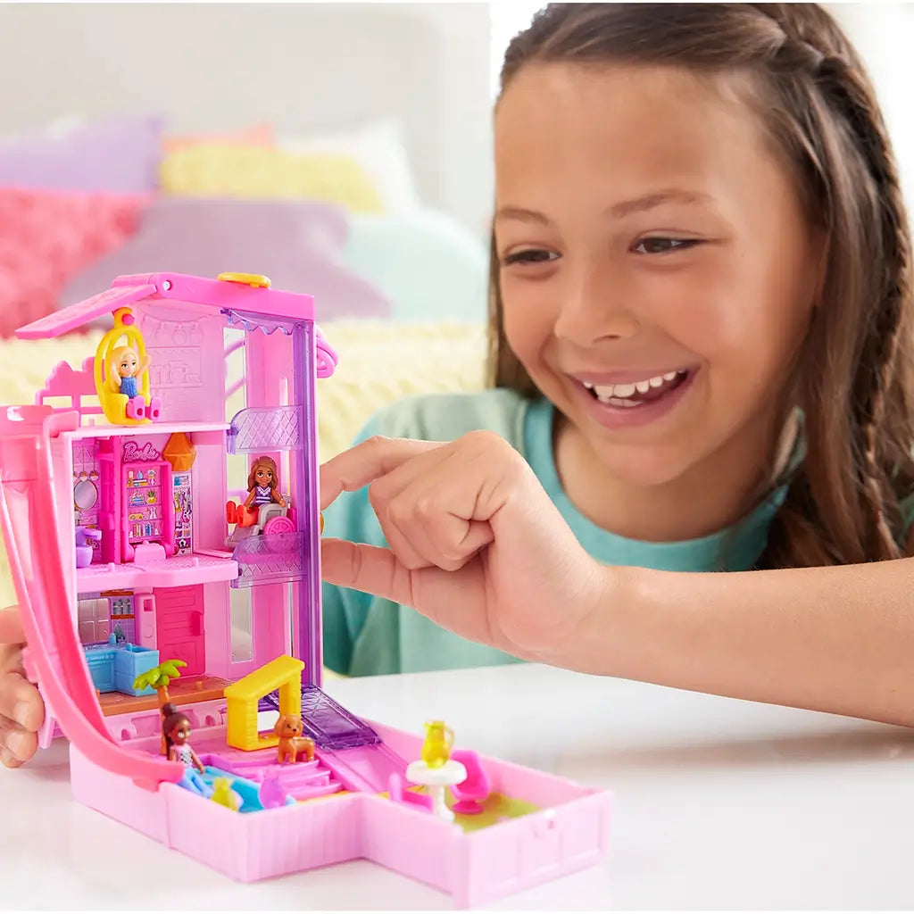 Child with brown hair plays happily with a bright pink Polly Pocket Barbie Dreamhouse Compact, featuring multi-level rooms, tiny dolls, and detailed miniature furniture.