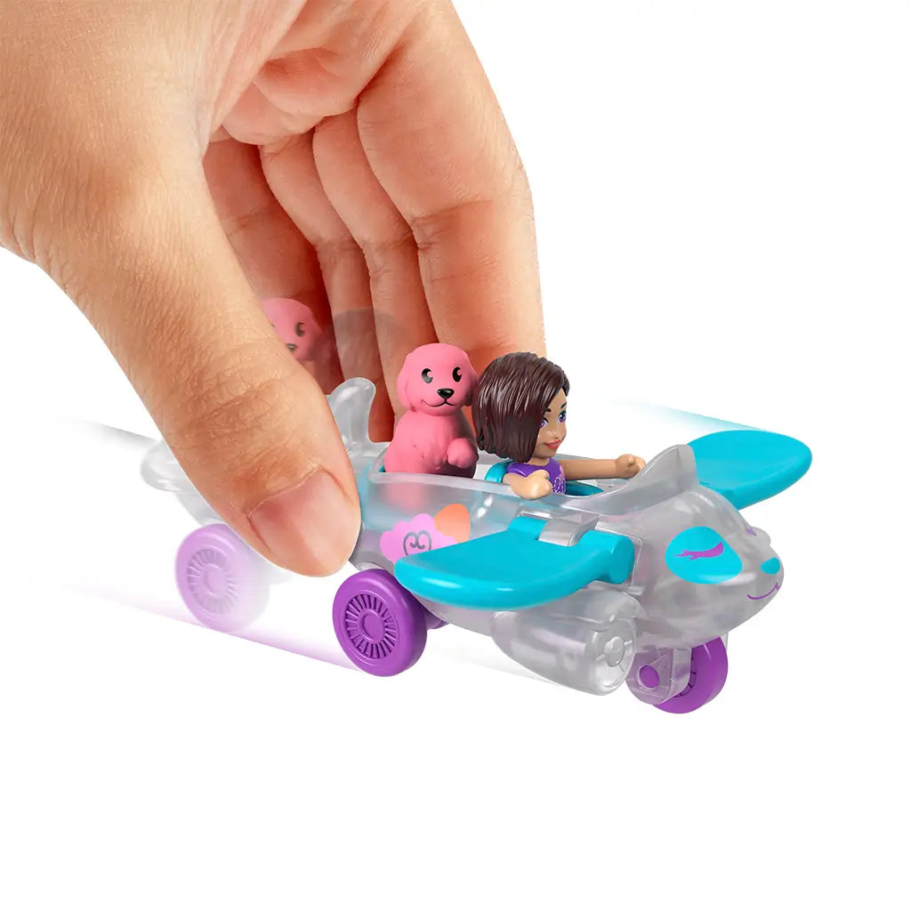 Hand pushing Polly Pocket silver airplane with blue wings, featuring seated Polly doll and pink dog figure, demonstrating toy movement against white background.