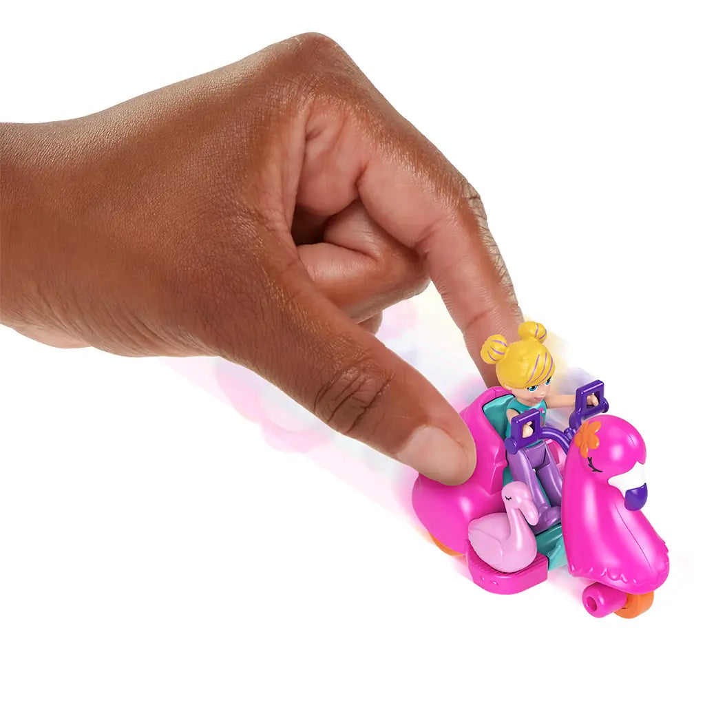 Hand pushing Polly Pocket bright pink flamingo scooter with teal seat, featuring Polly doll and small pink flamingo figure, demonstrating toy movement on white background.