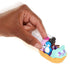 Hand pushing Polly Pocket teal dinosaur car with red-haired doll in the front seat and purple brontosaurus in the back, pink wheels rolling forward on a white background with motion blur.
