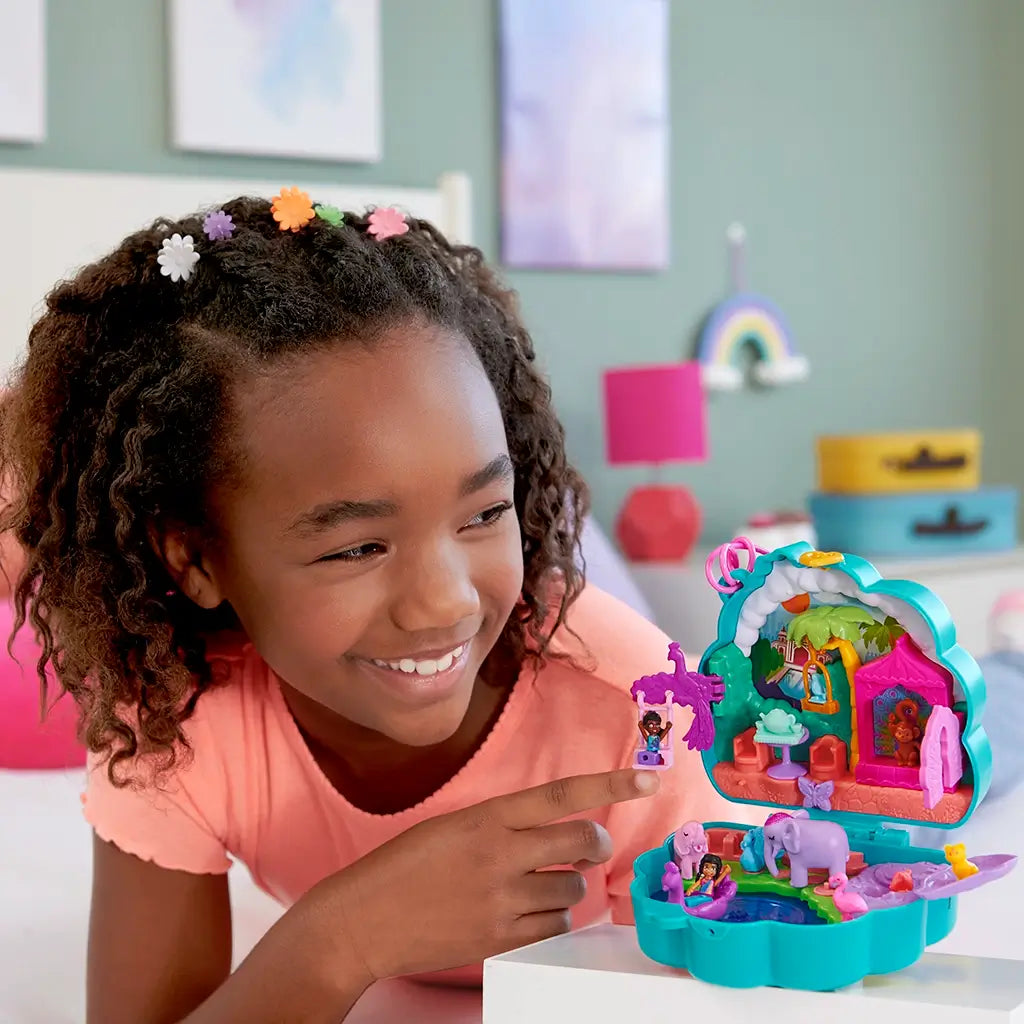 Smiling girl playing with Polly Pocket Peacock Garden playset, placing a doll on the purple peacock swing in a vibrant mini garden scene.