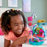 Smiling girl playing with Polly Pocket Peacock Garden playset, placing a doll on the purple peacock swing in a vibrant mini garden scene.