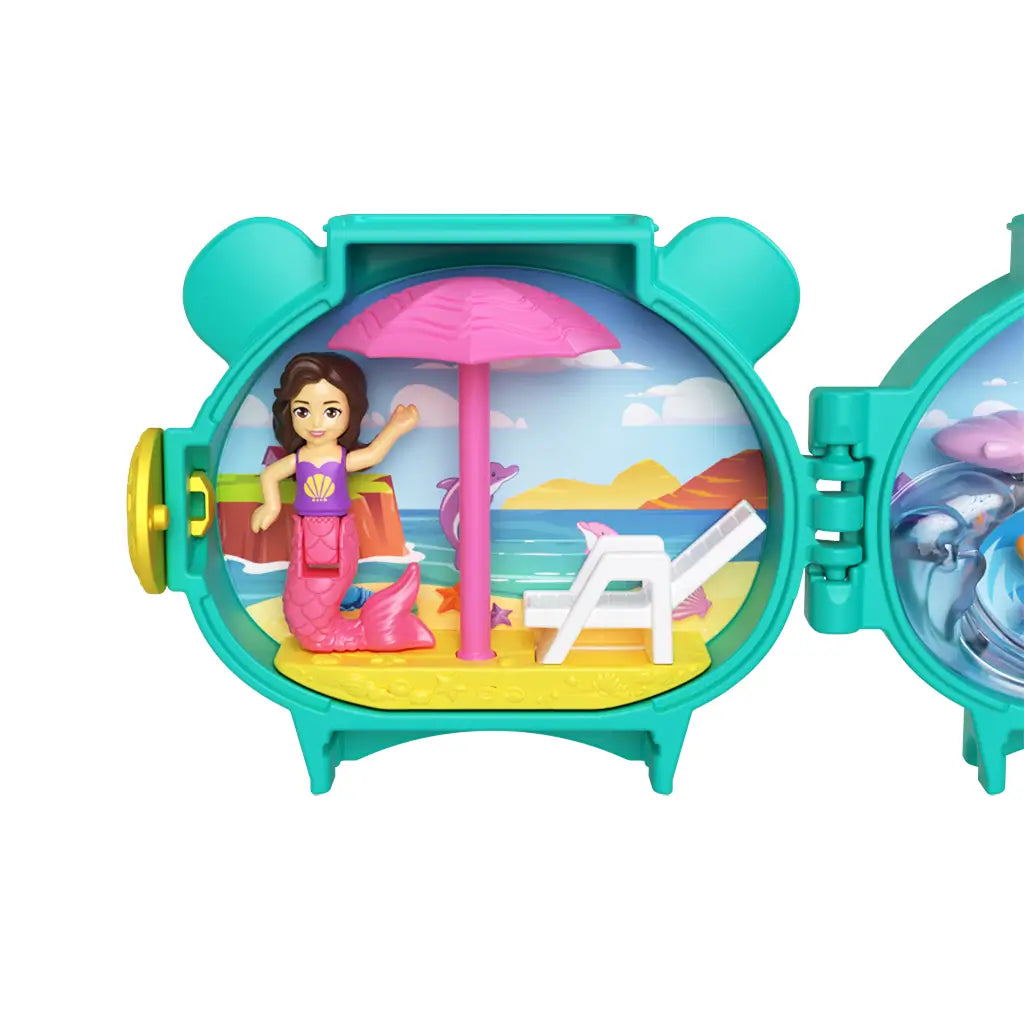Close-up of Polly Pocket Otter Locket playset beach side, featuring mermaid doll with pink tail, white lounge chair, and bright pink umbrella against ocean cliffs and dolphin-decorated backdrop.