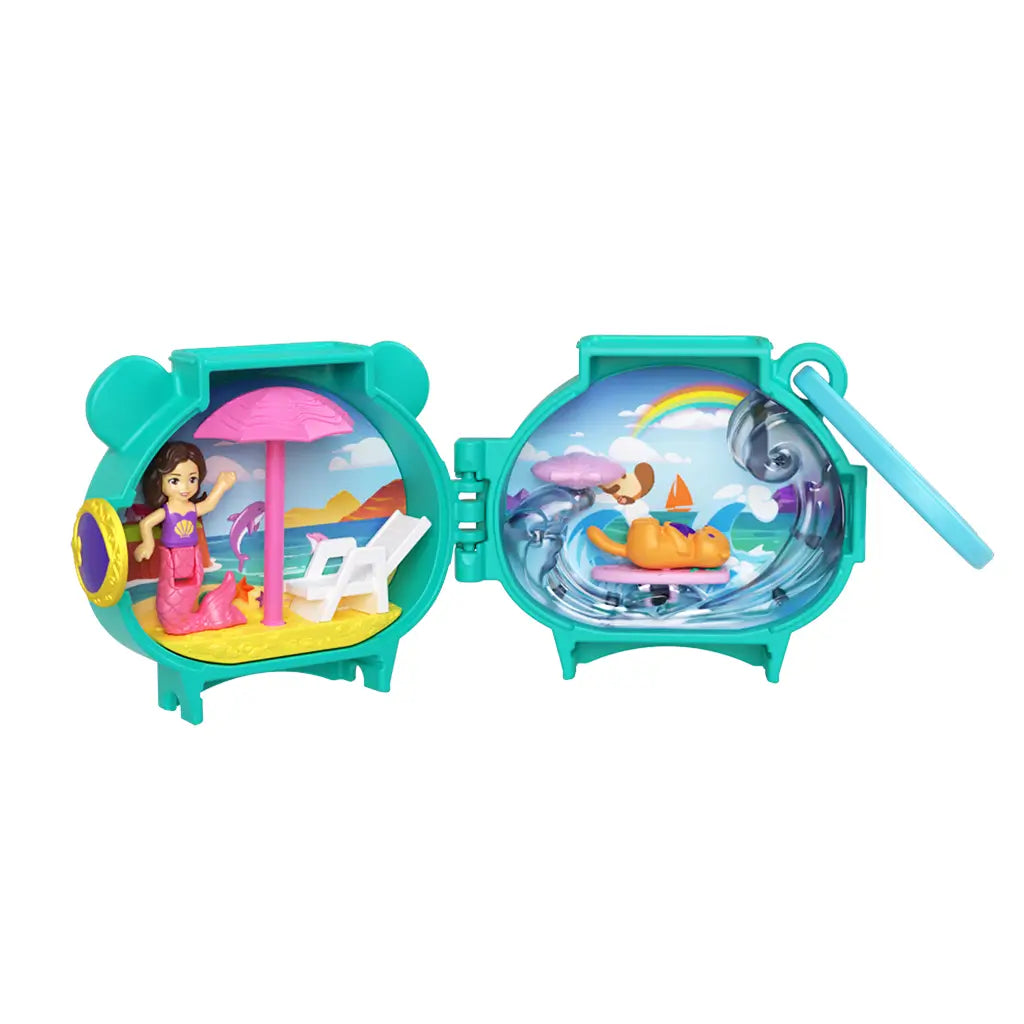Polly Pocket Otter Locket playset in teal plastic opens to reveal a colorful beach scene with pink umbrella, lounge chair, and a mermaid doll beside a wave-filled ocean backdrop.