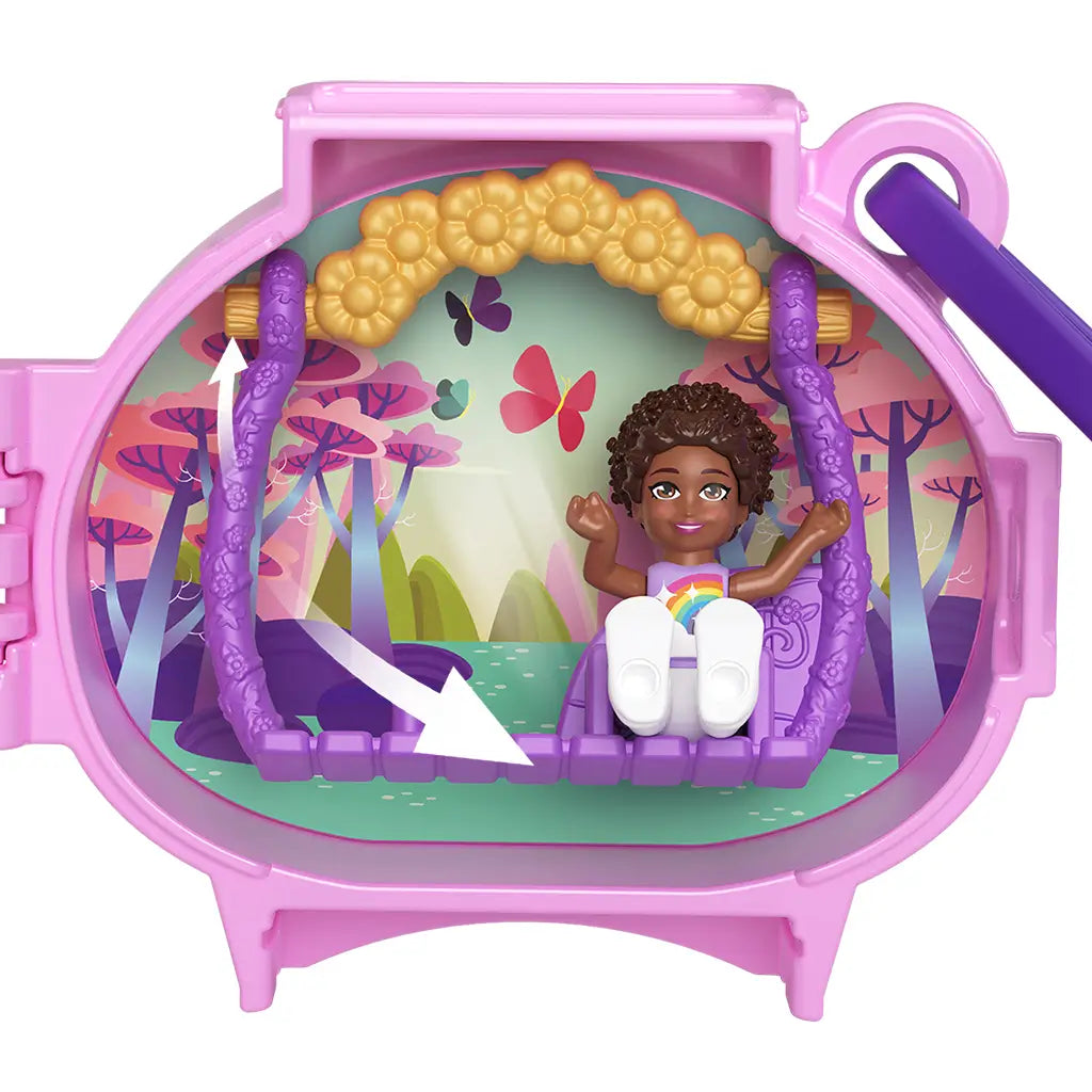 Open Polly Pocket unicorn locket showing mini doll sitting on purple swing under golden flower arch, with fantasy forest background of pink trees, butterflies, and pond.
