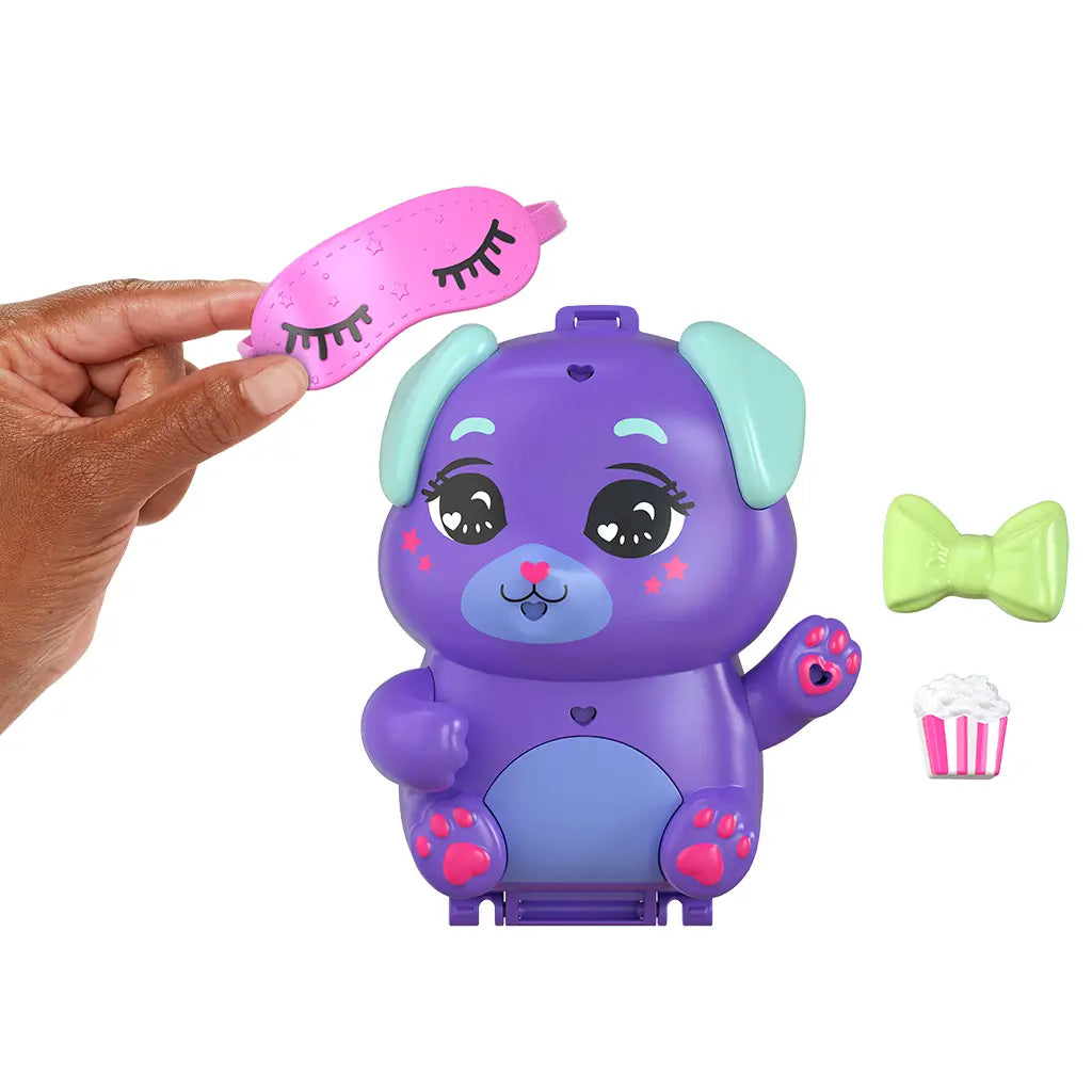 Hand placing pink sleep mask on purple Polly Pocket Puppy compact with green bow, removable popcorn accessory, and cute painted face details.