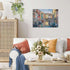 Completed Ravensburger Burano Italy 1000 piece puzzle displayed on wall above white sofa with colorful pillows and flowers, showing vibrant canal cityscape.