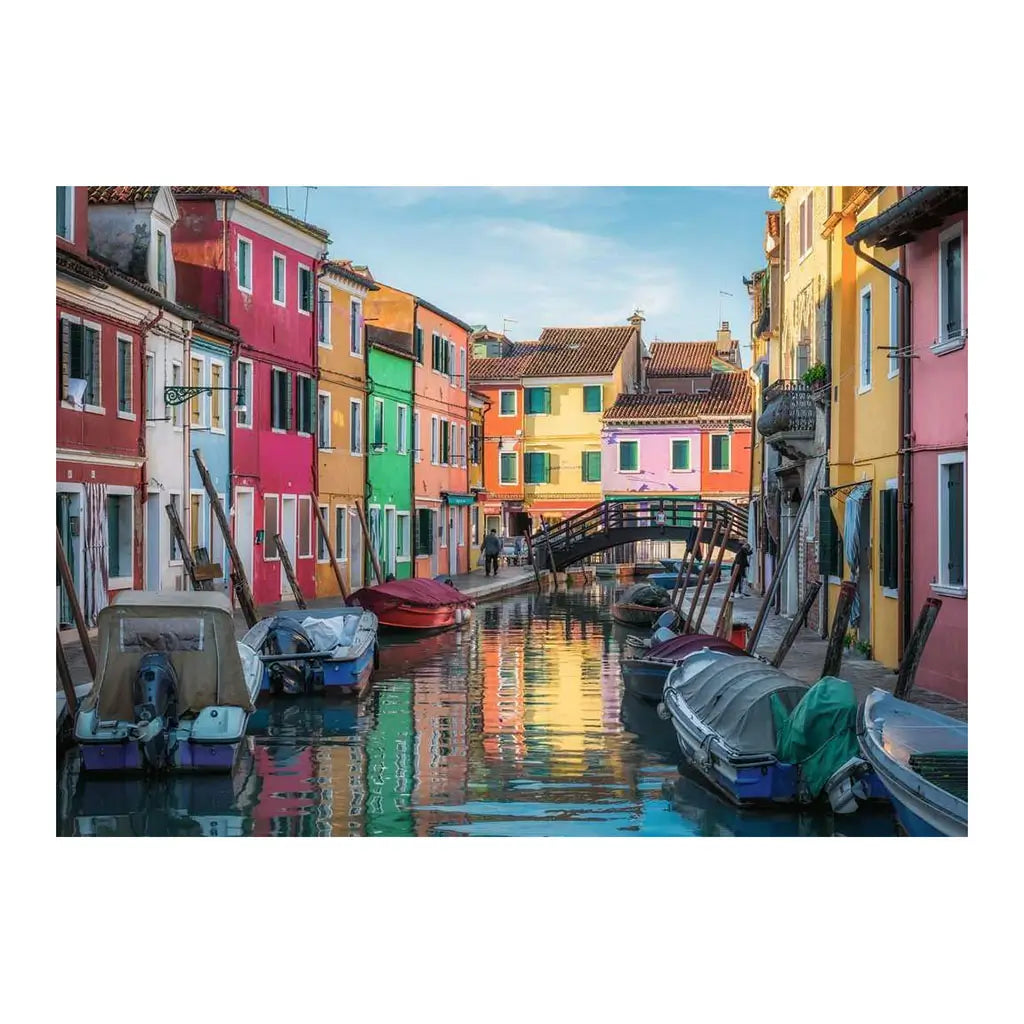 Detailed Ravensburger Burano Italy puzzle image featuring boats along a calm canal, pastel colored houses in pink, green, yellow, and orange, and arched footbridge.
