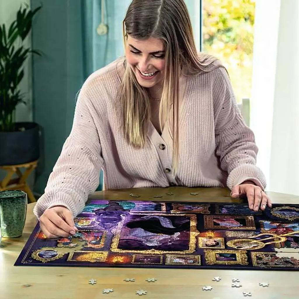 Smiling woman assembles Ravensburger Disney Villainous Ursula puzzle at a wooden table, surrounded by scattered pieces, highlighting vibrant purple artwork and golden frames.