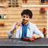 Smiling man adds final pieces to Ravensburger Ferrari SF90 Stradale 3D puzzle in a workshop with tools on the wall.