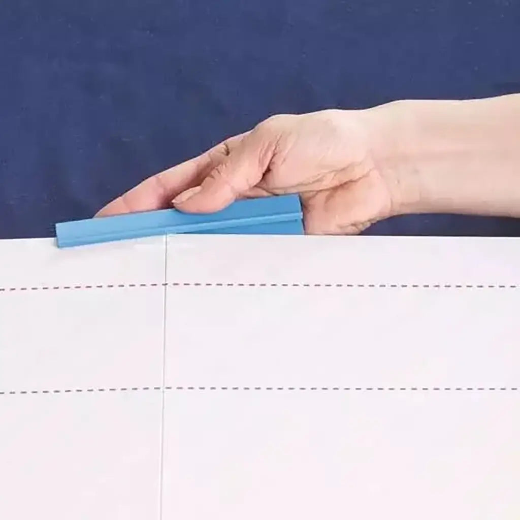 Hand attaching a bright blue plastic securing clamp to the foldable Ravensburger puzzle board edge, showing dotted crease lines for holding the board flat.