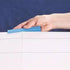 Hand attaching a bright blue plastic securing clamp to the foldable Ravensburger puzzle board edge, showing dotted crease lines for holding the board flat.