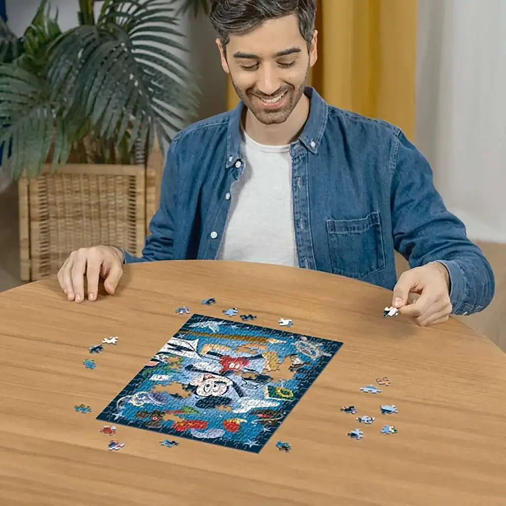Smiling man in denim shirt assembling Ravensburger Disney Mickey Mouse 300 piece puzzle on round wooden table, colorful blue design nearly completed in center.