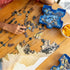Wooden table with partially completed jigsaw puzzle, scattered pieces, and blue Ravensburger sorting tray filled with pieces, next to a bowl of orange slices for a cozy puzzle setup.
