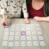 Young child and adult playing Marvel Spidey and His Amazing Friends matching game at a wooden table, turning over colorful cards with character images in a bright room.