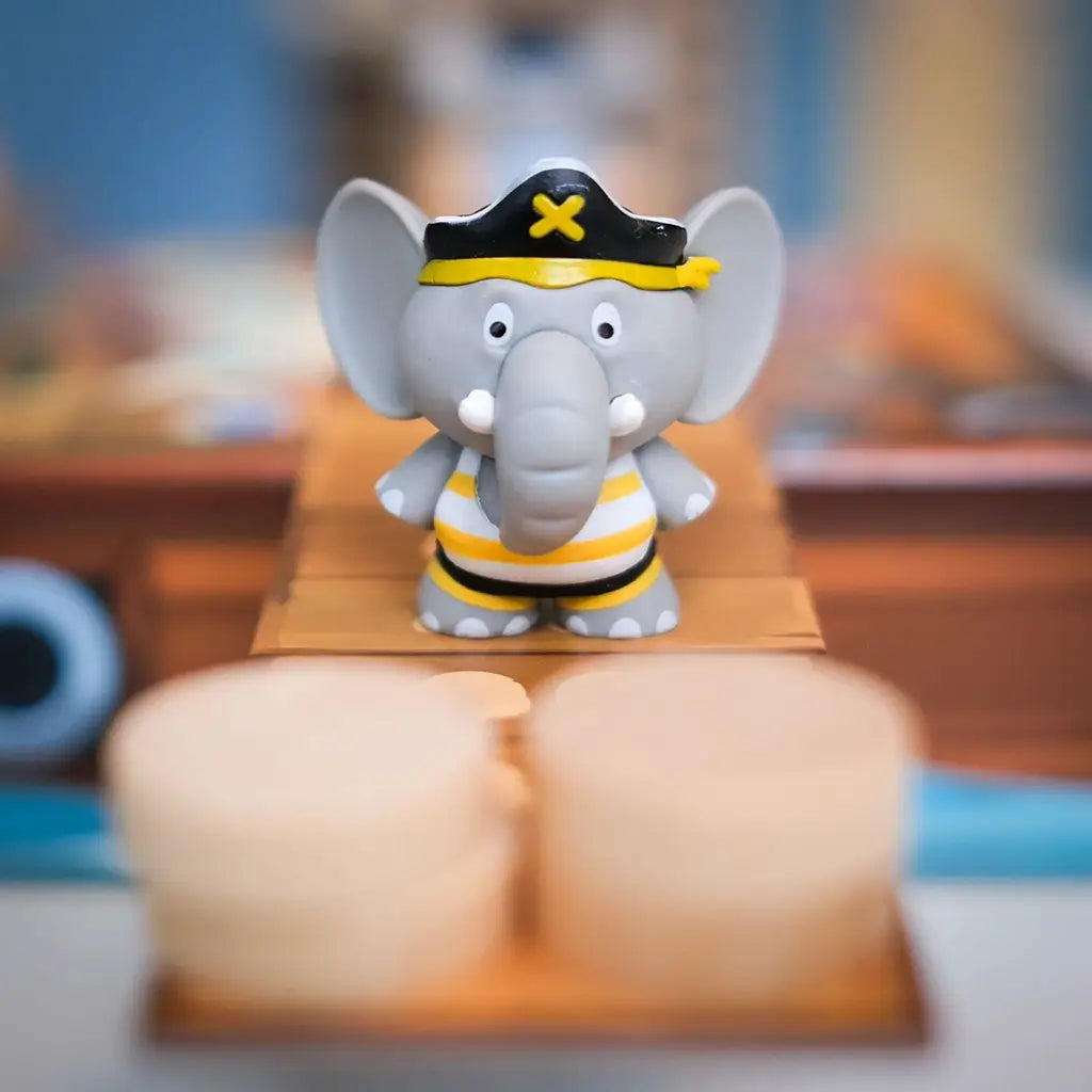 Close-up of a gray elephant figurine in a pirate hat and striped shirt standing on a cardboard plank in the board game Stomp the Plank.