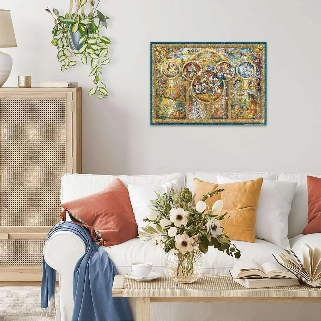 Completed Ravensburger Disney 1000 piece puzzle framed on wall above white sofa with colorful pillows and flowers, showing vibrant golden-framed Disney character montage.
