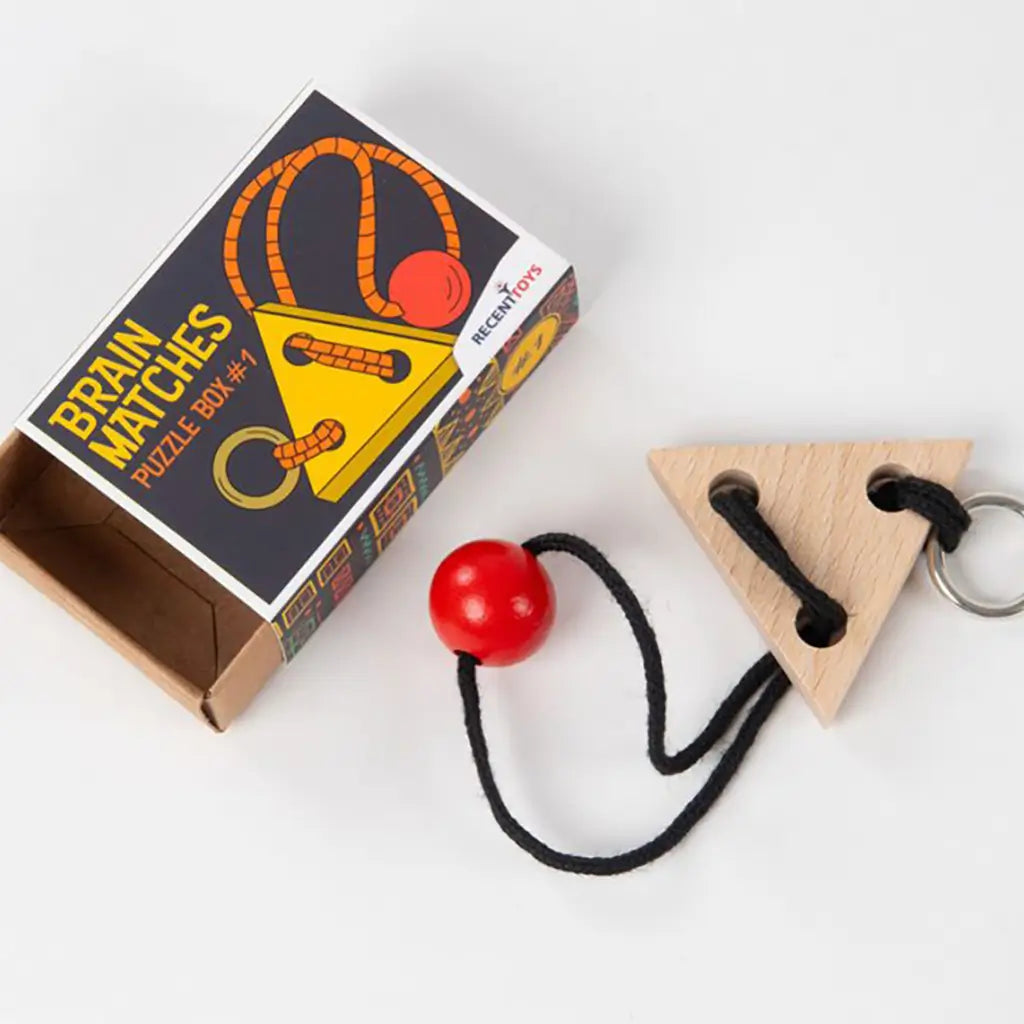 Wooden triangle puzzle with black cord and red bead shown next to its Brain Matches Puzzle Box #1 packaging with illustrated design and open drawer box.