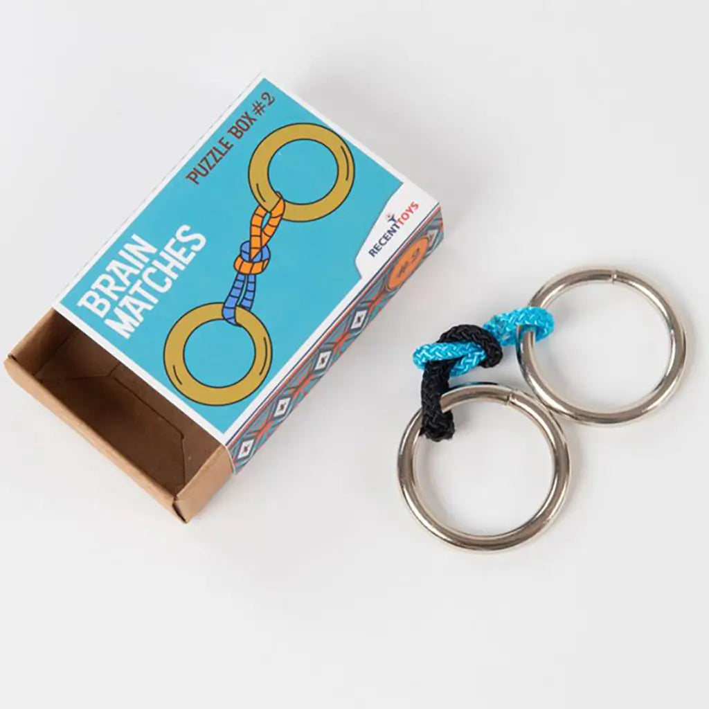Metal double ring puzzle connected with blue and black rope, placed beside Brain Matches Puzzle Box #2 packaging featuring illustrated interlocking rings.