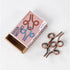 Bronze-colored interlocking metal wire puzzle with looped shapes, positioned beside Brain Matches Puzzle Box #6 packaging with matching abstract design.