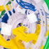 Rubik’s Tracks 3D gravity maze close-up reveals a silver metal ball resting on a bright yellow plastic ramp beside white supports and blue rails inside the transparent sphere.