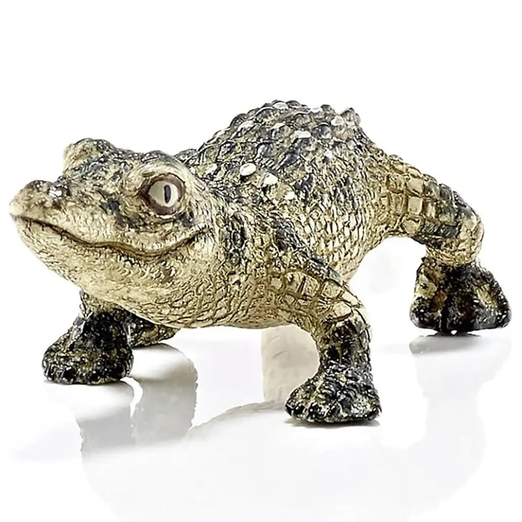 Schleich baby alligator toy close up showing olive green and tan textured plastic scales, rounded snout, sculpted eyes and ridged back, crafted for educational animal play and detailed display on a clean white surface.