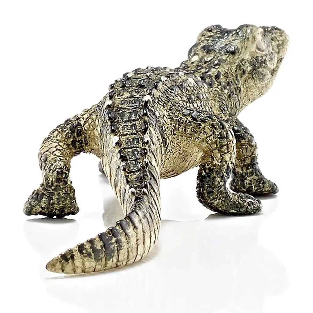 Schleich baby alligator figurine displaying olive green and tan textured plastic, rear angled crawling stance, segmented tail and raised scale ridges, designed as a durable wildlife toy against a plain white background.