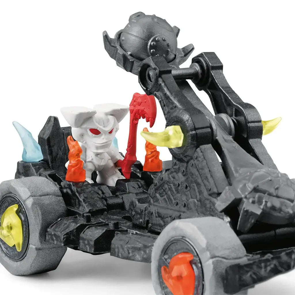 Schleich Eldrador catapult close-up shows dark gray stone-like plastic texture, articulated launching arm holding a round projectile, bright crystal details, and a white mini creature figure with red eyes seated inside.