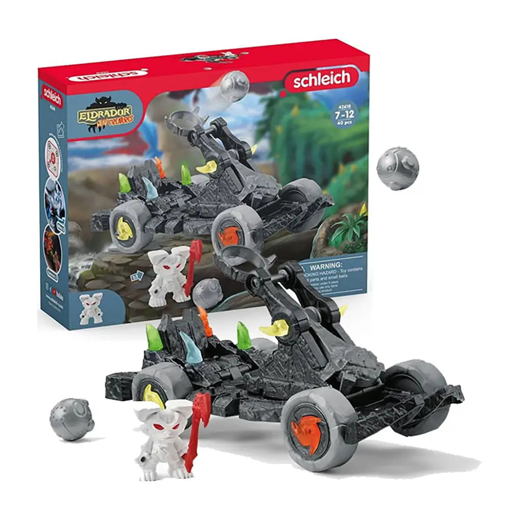 Schleich Eldrador catapult playset features dark gray rock-textured plastic, rugged wheeled vehicle form, hinged throwing arm, colorful crystal accents, and a white mini creature figure, shown with retail packaging on a white background.