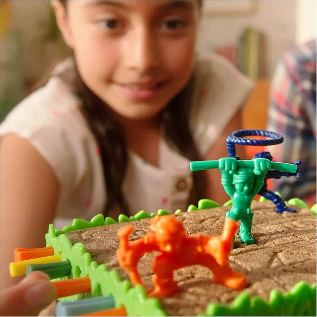 Smiling girl focuses on Sink N’ Sand board game, moving bright orange and green explorer figures across sand-filled platform supported by colorful sticks in play.