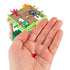 Hand holding small red gem piece from Sink N’ Sand game with jungle sand platform and colorful explorer figures visible in the background.