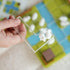 Hand holding a transparent L-shaped puzzle piece with two white sheep, with the green and blue farm-themed game board visible in the background during play.