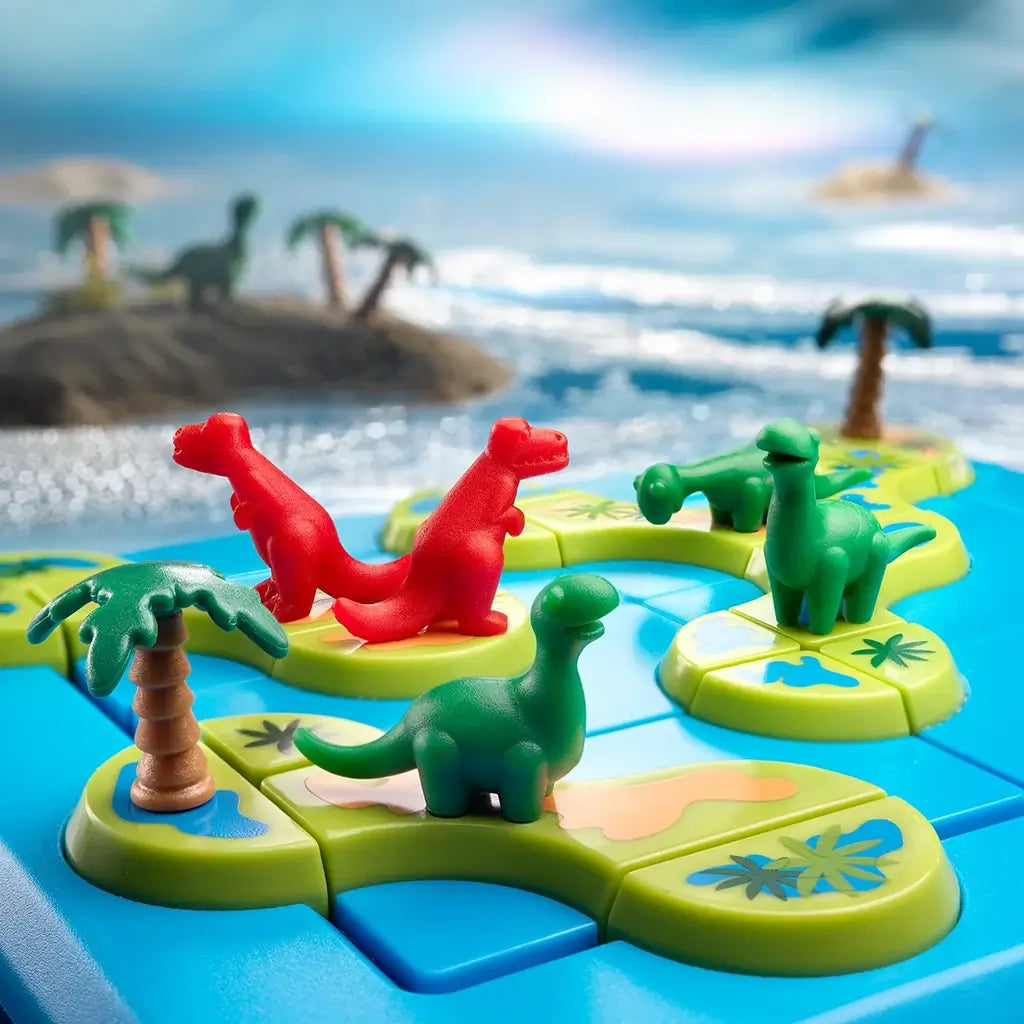 Close-up of Smart Games Dinosaurs Mystic Islands puzzle board showing green and red dinosaur figures on bright island tiles with palm trees, set against a blurred ocean backdrop.