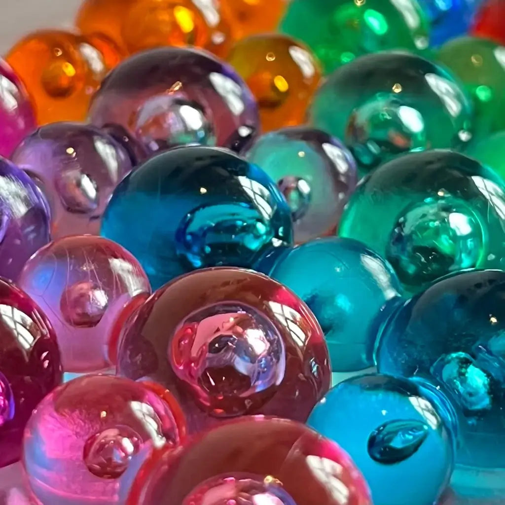 Close-up macro shot of glossy transparent bubble puzzle pieces in bright shades of pink, orange, blue, green, and purple, highlighting texture, reflections, and rounded surfaces.