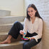 Young woman sitting on stairs in casual clothes, smiling while playing with the colorful SmartGames IQ Hexagon puzzle, holding a bright blue piece above the board.