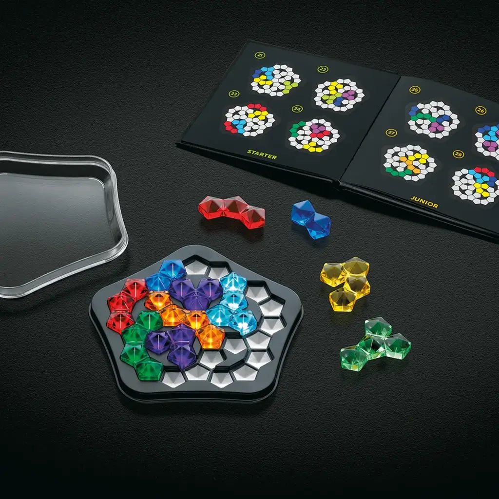 Open SmartGames IQ Pentagon set showing the black tray, bright gem-like puzzle pieces in various colors, a clear lid, and a challenge booklet with diagrams.