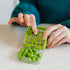 Green plastic SmartGames IQ Mini brainteaser with round puzzle pieces being placed by hand on a smooth table, showcasing its tactile logic challenge design.