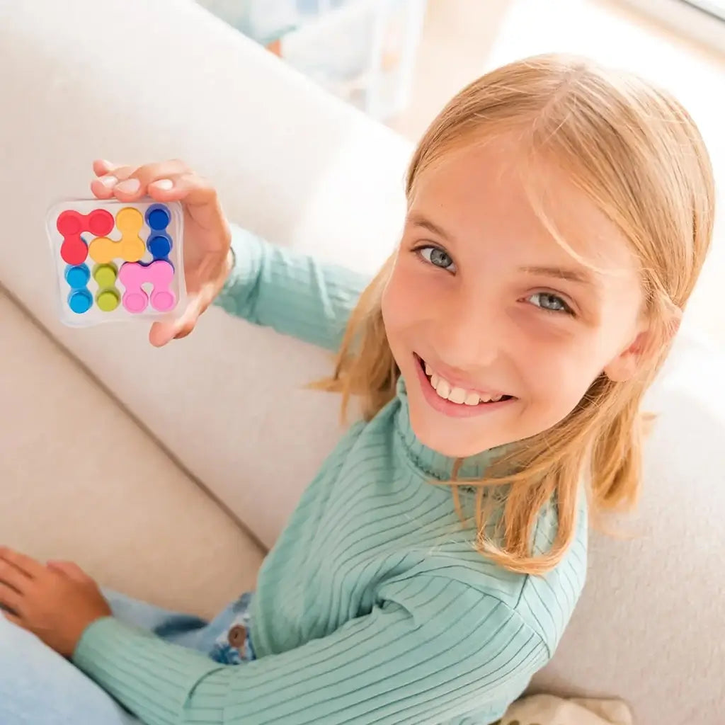 Smiling young girl in a teal sweater holding a small Reverso Fidget Puzzle, showing brightly colored interlocking pieces inside a compact transparent game case.